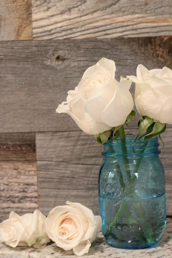 Blue Mason jars with shabby roses in front of a barn wood wall, easy planked wall DIY from RefreshRestyle.com