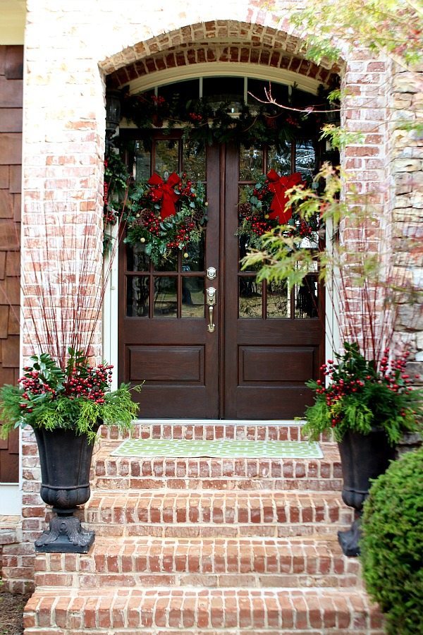 Welcome to our home at Christmas, the double doors have matching wreaths and garland above with natural elements in the flower pots.