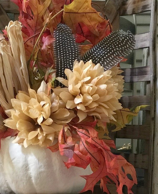 Fall leaves in a white pumpkin with feathers and mums