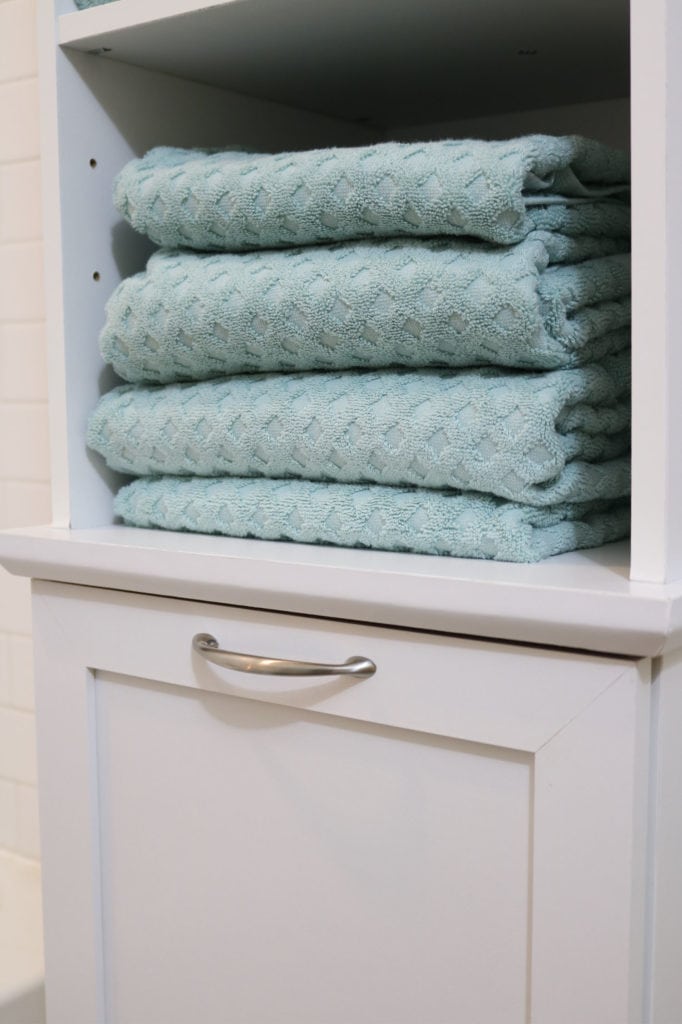 Bathroom storage with a hamper and large aqua teal towels